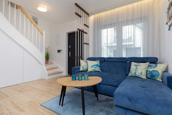 Un salon moderne avec un canapé bleu, un escalier en bois et une table basse ronde en bois.