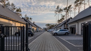 Une rue résidentielle fermée par des portails, bordée de voitures garées et de maisons.