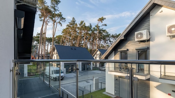Un immeuble résidentiel moderne doté d’un balcon, d’un garage et offrant une vue sur une rue bordée de voitures garées et d’arbres.