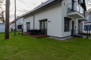 Une maison moderne à deux étages, dotée d’un balcon, d’une terrasse avec mobilier d’extérieur et d’une pelouse bien entretenue.