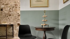 Zona pranzo con due sedie nere, un tavolo rotondo e un piedistallo per dolci, oltre a un quadro appeso al muro.