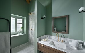 A bathroom with a window, a shower, a sink with a mirror, and towels.