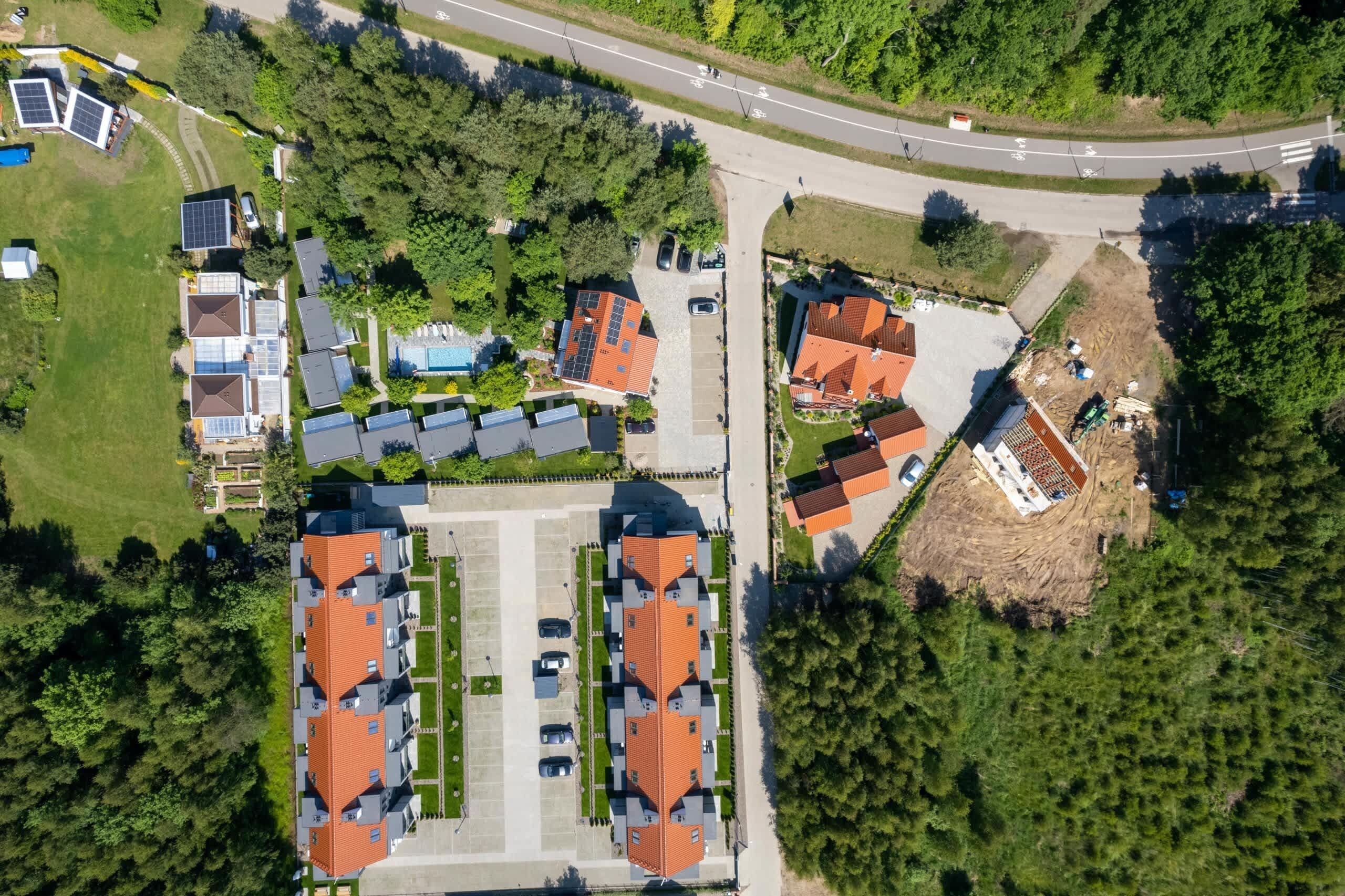 Oversigtsbillede af et boligområde med flere huse, en parkeringsplads og en vej.