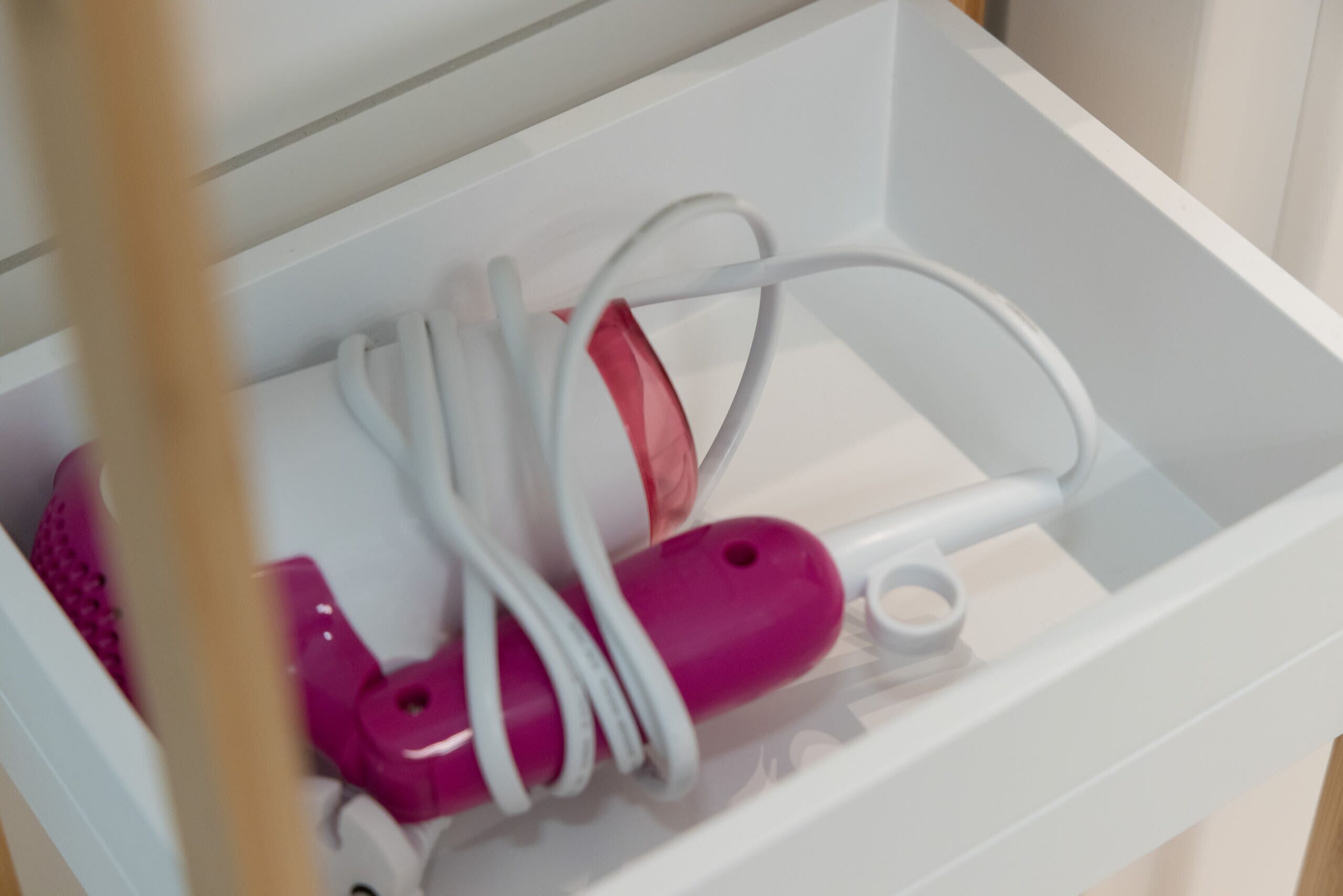 Een witte lade met een roze en witte elektronische apparaat, mogelijk een haardroger, en een witte kabel.