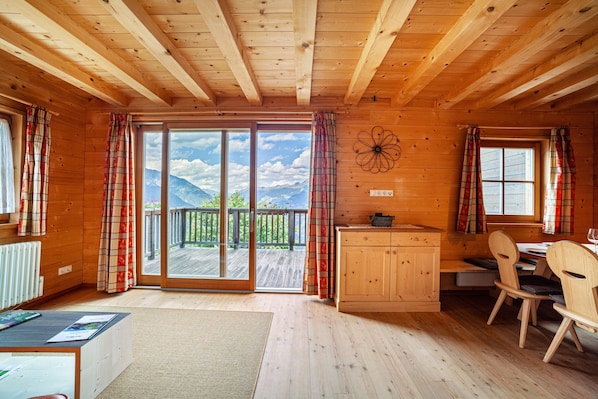 A wooden cabin interior with a dining area, wooden cabinets, and a view of a deck and mountains.