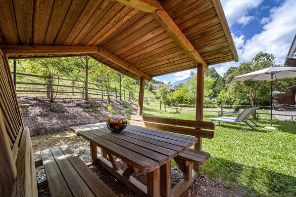 Un pavillon en bois, équipé d’une table de pique-nique et de bancs, entouré d’une pelouse et d’une clôture en bois.