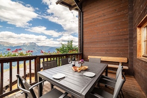 A wooden deck with a table set for two, chairs, and a bench.