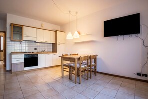 A modern kitchen with white cabinets, a dining table with chairs, and a flat-screen TV mounted on the wall.