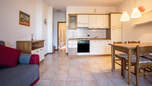 Un ambiente compatto con angolo cottura, zona pranzo e un letto con cuscini.