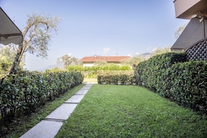 A pathway leading to a building with a red-tiled roof, surrounded by well-maintained hedges and a clear sky.