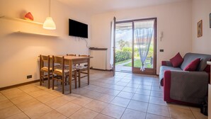 Una stanza con un tavolo da pranzo, sedie, una TV a parete, un divano e una porta vetrata scorrevole che dà su un giardino.
