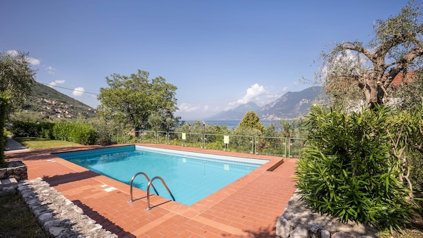 Una piscina rettangolare con acqua cristallina, circondata da un patio in mattoni, con vista sul mare e sulle montagne sullo sfondo.