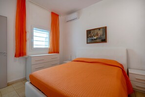 Une chambre à coucher avec un lit, une fenêtre avec des rideaux, une table de chevet, une commode et un tableau accroché au mur.