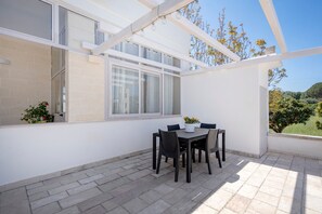 Une terrasse couverte avec une table et des chaises, une plante en pot et une vue sur l’extérieur.