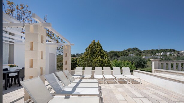 En takterrass med solstolar, en pergola och utsikt över en sluttning med träd och byggnader.