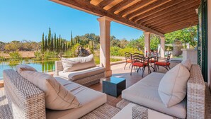 Un patio exterior con mobiliario de mimbre, una mesa de piedra y vistas a un lago y árboles.