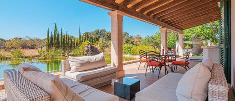 An outdoor patio with wicker furniture, a stone table, and a view of a lake and trees.