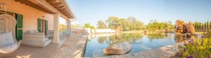 Una piscina con un elemento rocoso, asientos al aire libre y una pérgola.