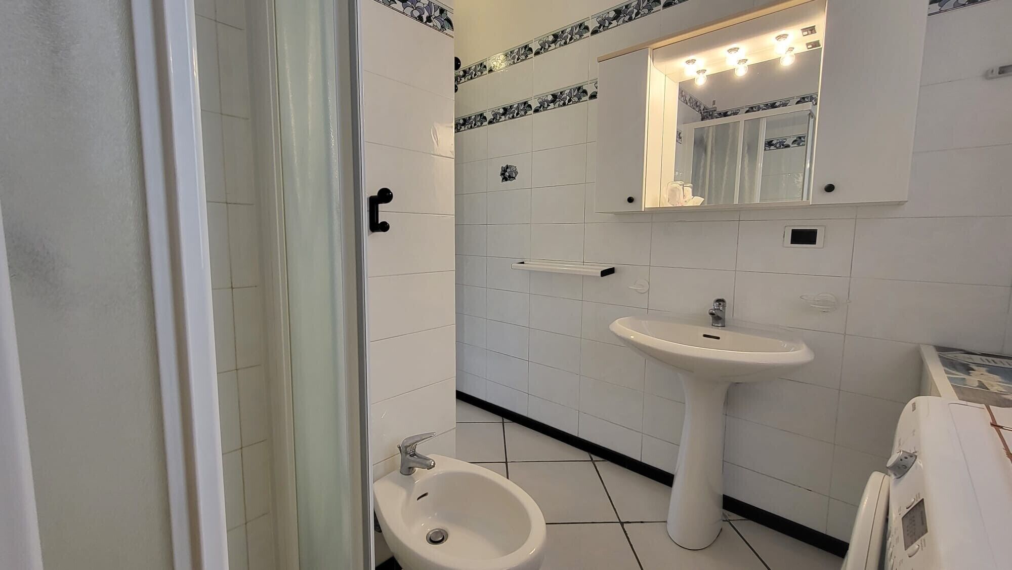 A bathroom with a pedestal sink, a mirror with lights, a bidet, and a toilet.