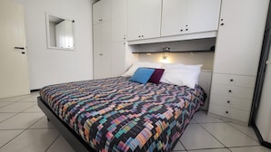 A bedroom with a bed, a wardrobe, a mirror, and a nightstand.