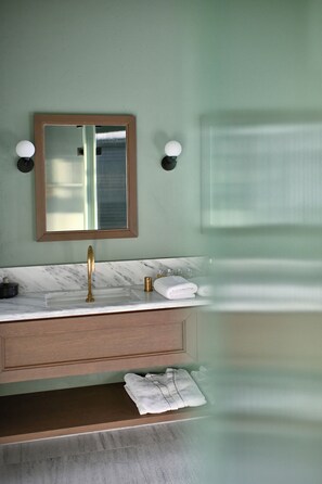 Une salle de bain avec un lavabo en marbre, un robinet doré, un miroir avec un cadre en bois et deux appliques murales.