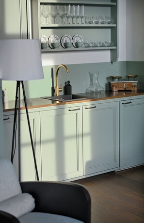 Une cuisine avec des meubles de couleur vert clair, un plan de travail en bois et un évier doté d’un robinet doré.