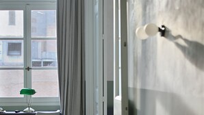 A room with a wooden floor, a desk with a chair, a window with curtains, and a door with a light fixture.