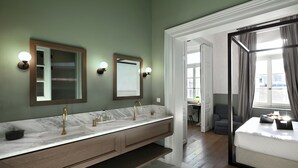 A modern bathroom with a marble vanity, two mirrors, and a large window with curtains.