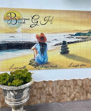 A mural of a woman on a beach with the words "Boutique Guest Home" and "Live well, Love much, Laugh often" on a tiled wall.