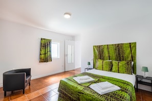 A bedroom with a bed, a chair, a nightstand, and a window.