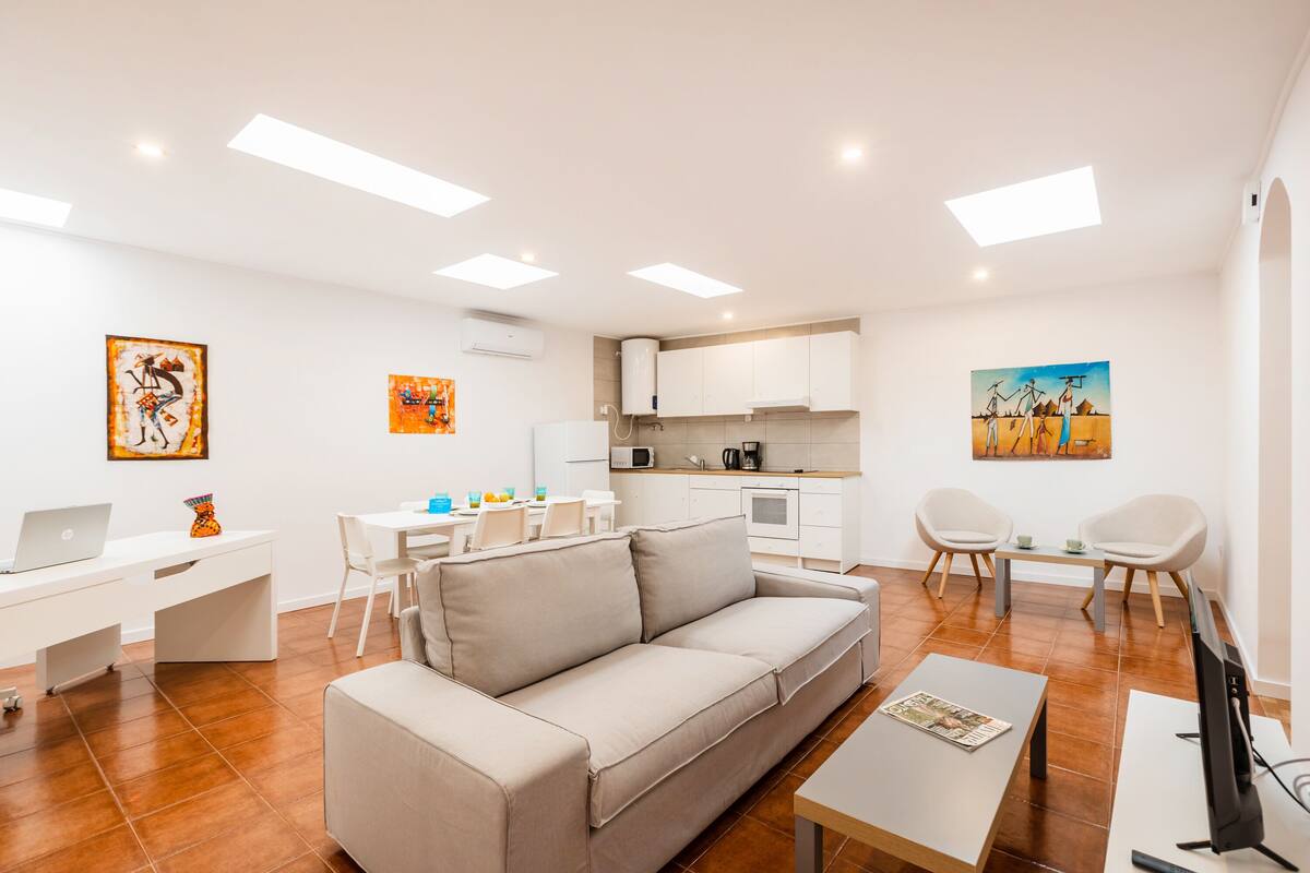 A modern living room with a sofa, a dining table, and a kitchen area with cabinets and a microwave.