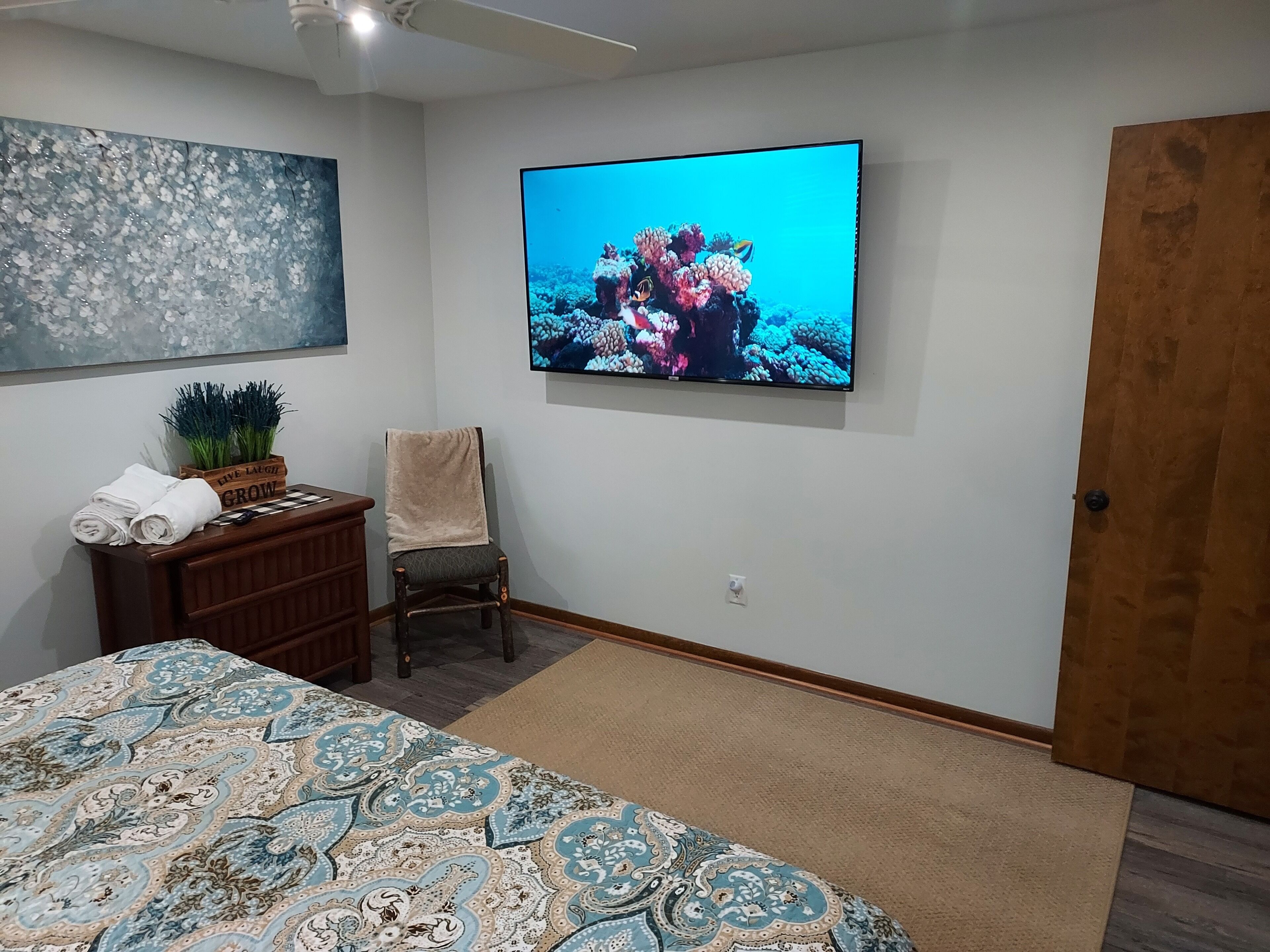 Een slaapkamer met een bed, een stoel, een dressoir, een televisie en een deur.