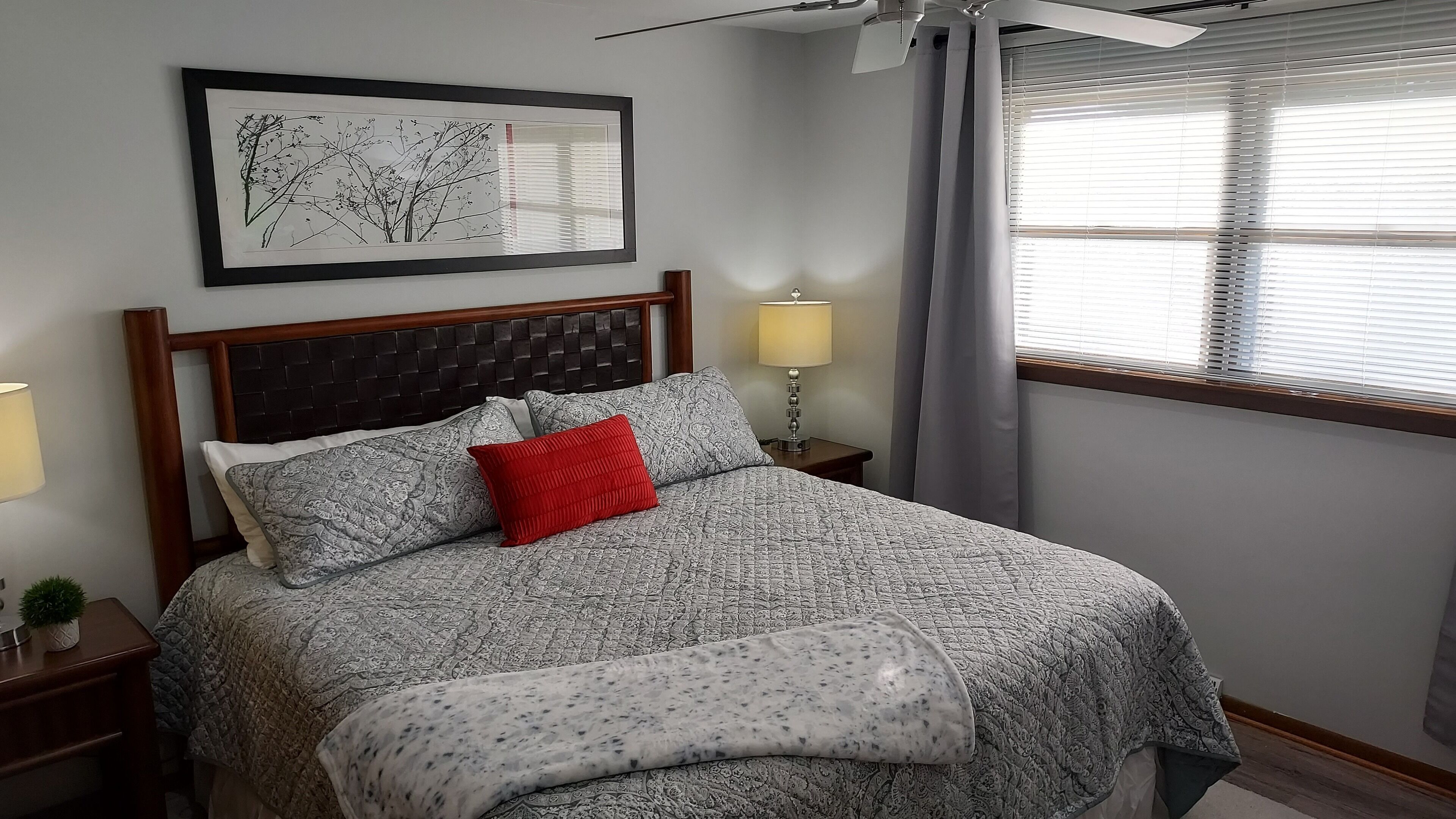 A neatly made bed with patterned bedding, a red pillow, and a bedside lamp.