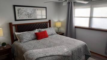 A neatly made bed with patterned bedding, a red pillow, and a bedside lamp.