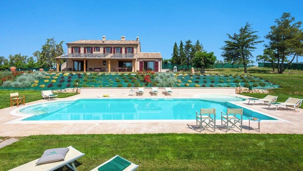 Ein großer Pool mit Liegestühlen und ein gepflegter Garten vor einem zweistöckigen Haus.