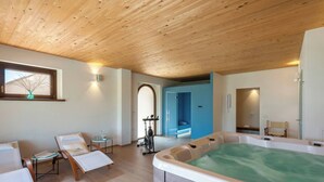 Ein Wellnessraum mit Holzbalkendecke, Whirlpool, Fitnessfahrrad und zwei Liegestühlen.