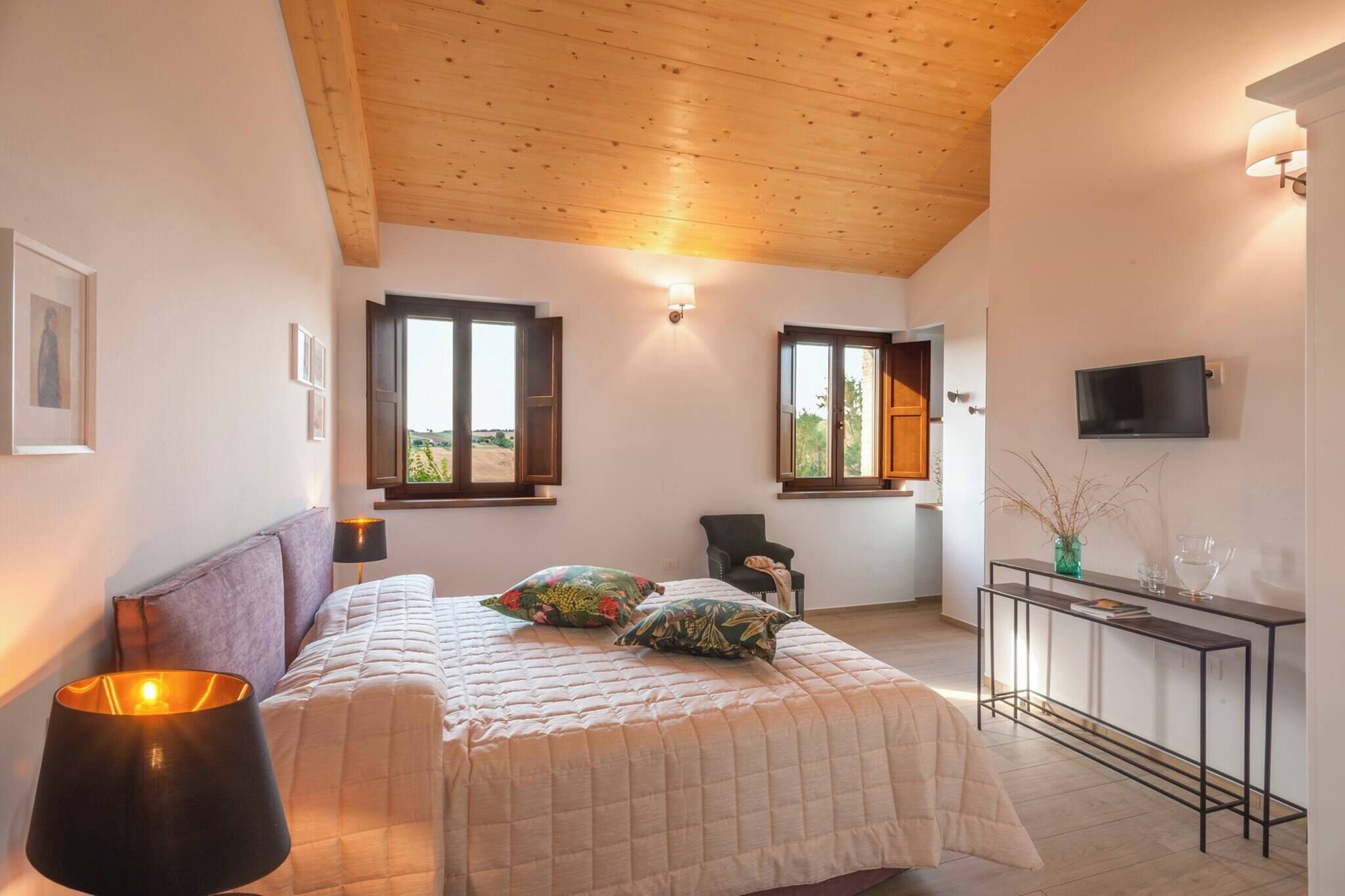 A bedroom with a bed, bedside lamps, a chair, a TV, and a window with a view.
