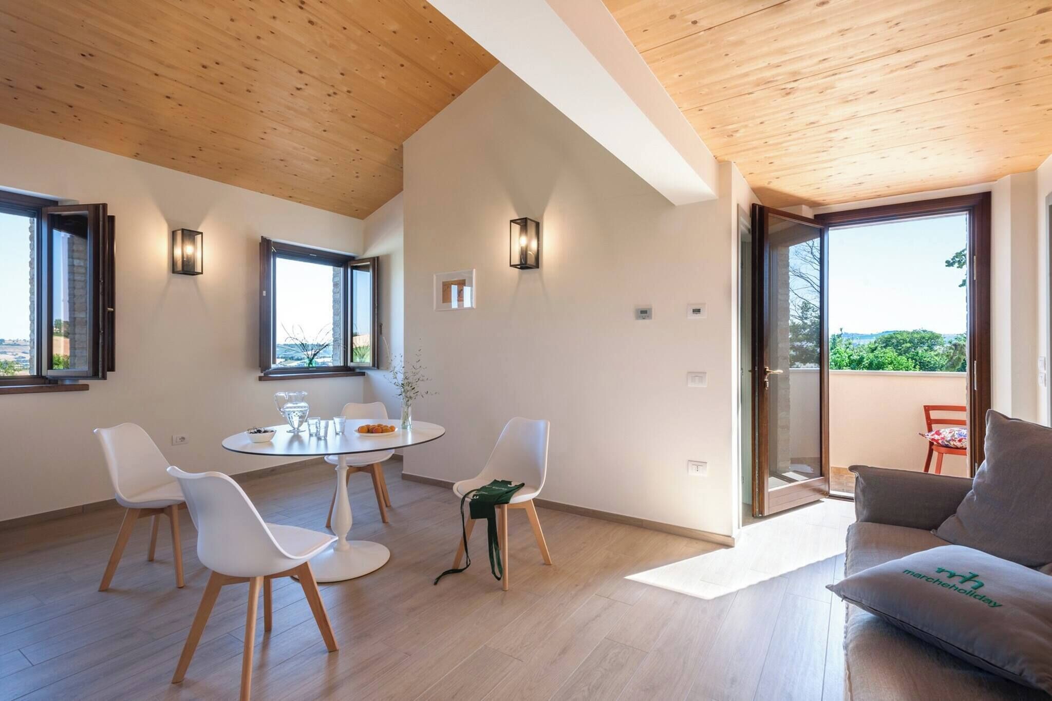 A modern living room with a round table, white chairs, a grey sofa, and a balcony with a view.