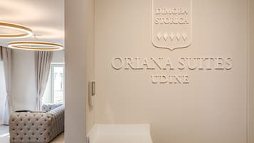 A hotel interior with a sign for 'Orlana Suites Udine' and a tufted sofa in the foreground.