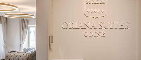 Interior de un hotel con un cartel que dice 'Orlana Suites Udine' y un sofá con textura en primer plano.