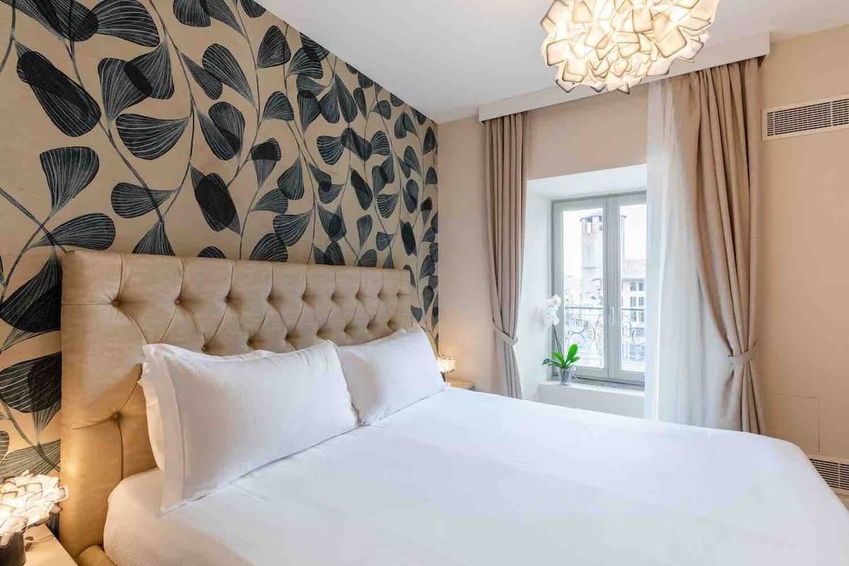 Ein Hotelzimmer mit einem gebogenem Kopfteil, einem großen Bett, einem Fenster mit Vorhängen und einem dekorativen Wandmuster.