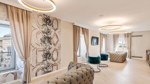 Un saló modern amb un llit gran modular, un pouf amb guarnició i un butac armchair color aquamarina. L'espai destaca per una finestra gran amb cortines, un mural decoratiu i un lluminari de sostre circular.