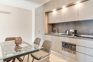 A modern kitchen with a glass dining table and chairs, a coffee machine, and a marble backsplash. - Oriana Homèl Udine (Udine)