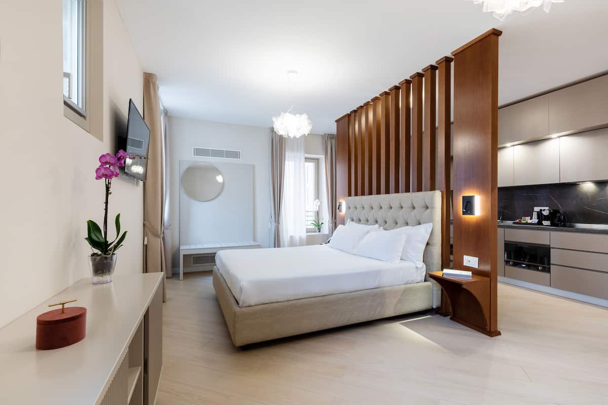 Ein modernes Schlafzimmer mit einem großen Bett, einem Nachttisch, einem an der Wand montierten Fernseher und einer Küchenzeile mit Arbeitsplatte und Schränken.