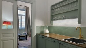 Une cuisine avec un évier, une fenêtre avec des rideaux et une étagère avec des verres.