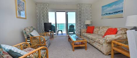 A living room with a sofa, chairs, a coffee table, a TV, and a balcony with a view.