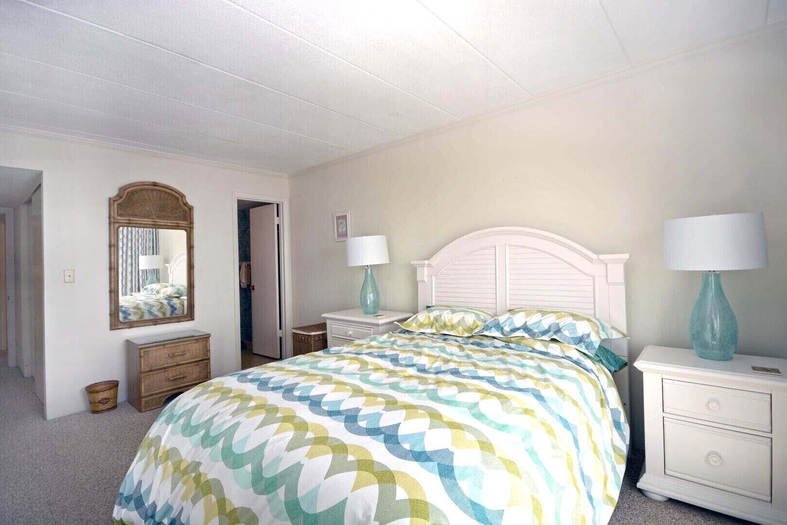 A bedroom with a bed, two nightstands, a dresser, a mirror, and a door.