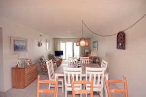 Un coin repas avec une table et des chaises en bois, un téléviseur en arrière-plan et une lampe décorative suspendue au plafond.