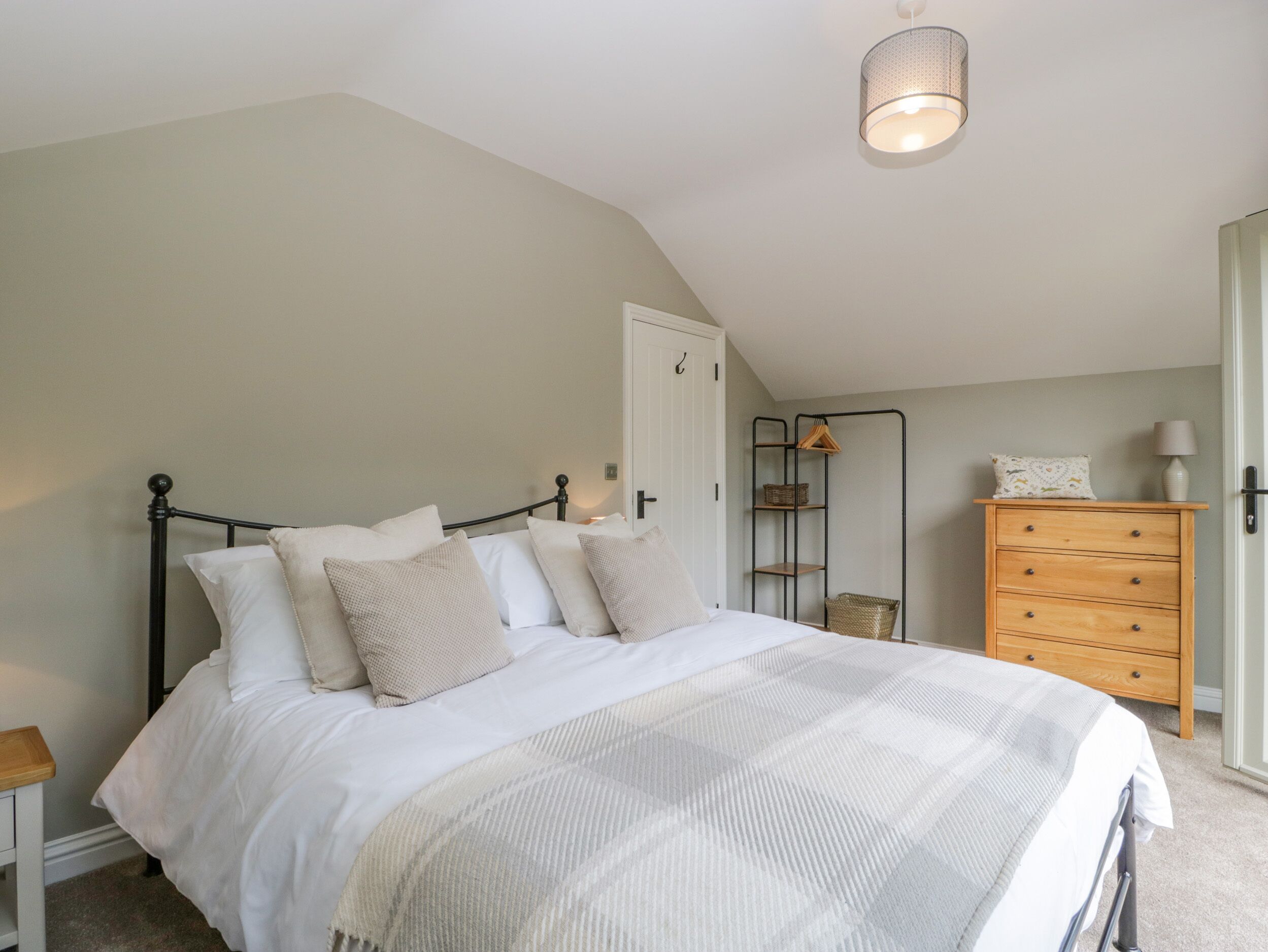 A bedroom with a bed, a dresser, a nightstand, a hanging light fixture, and a door.