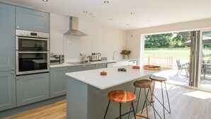 Uma cozinha moderna com armários cinza, uma ilha central com banquetas e vista para o exterior por grandes portas de correr.